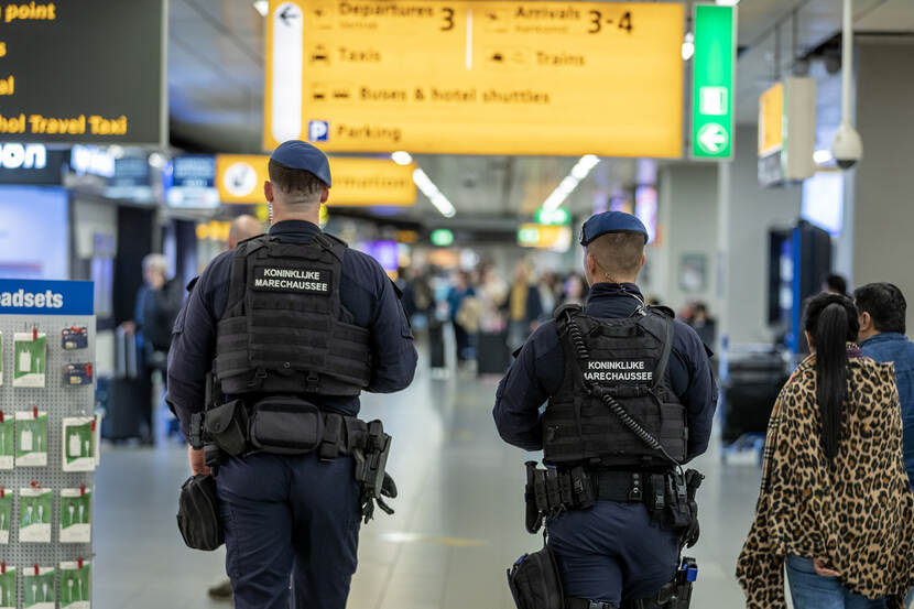 Twee marechaussees, op de rug gezien, lopen rond op Schiphol.
