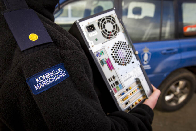 Marechaussee met een computerkast in de hand.