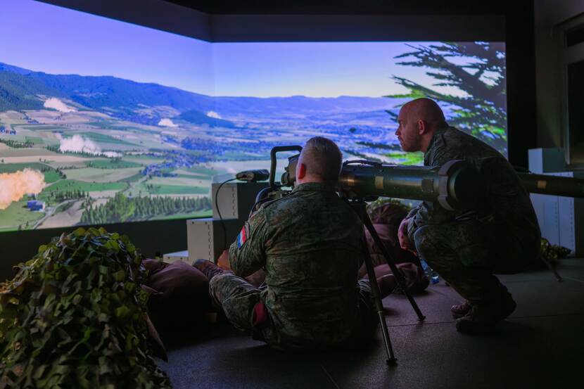 twee militairen zijn aan het werk in het nieuwe simulatiecentrum bij een scherm met een afbeelding van een landschap