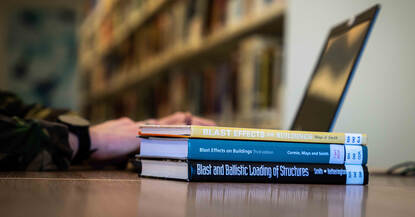 Militair achter laptop met stapel boeken over munitietechniek