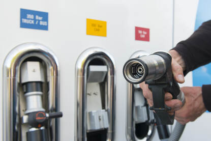 Iemand trekt de slang uit een pomp van een waterstof tankstation