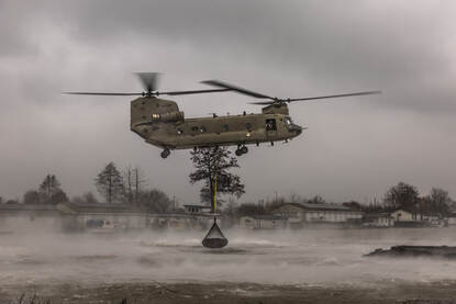 Een Chinook dropt een net vol stenen in het water.