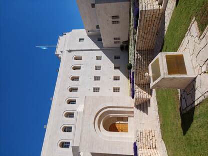 Een beige, stenen gebouw met halfronde ramen met op de achtergrond een helderblauwe lucht.