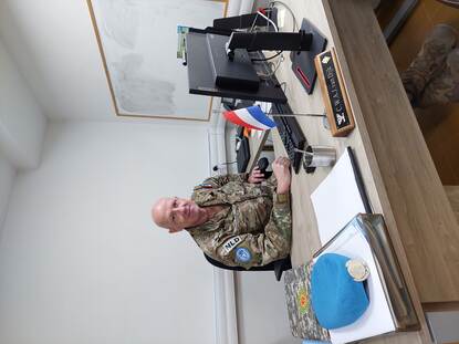 Een wit kantoor met whiteboard en bureau waar kolonel Van Dijk aan zit.