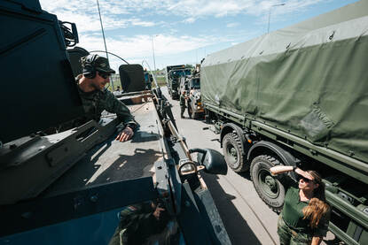 Een militair praat vanuit hoogte van zijn voertuig met een collega die naast het voertuig staat.