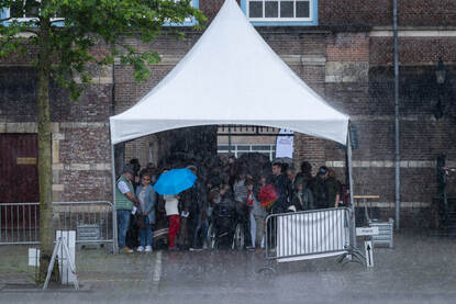 Mensen schuilen onder een tentje voor hevige regenval op de KMA.
