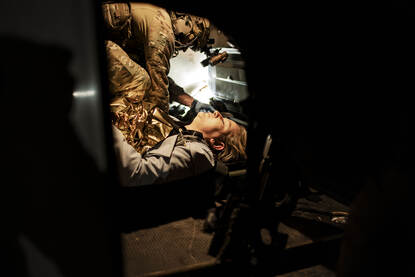 Een vrouw ligt op de grond en wordt geholpen door een Belgische militair.
