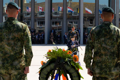 Tweede Wereldoorlogveteraan Max Wolff wordt in een rolstoel richting een bloemenkrans gereden door een luitenant-kolonel.