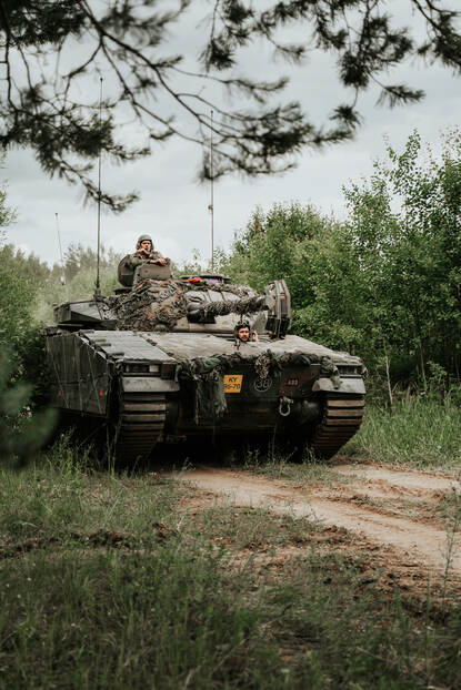 Close-up van een gecamoufleerd CV90-infanteriegevechtsvoertuig die komt aanrijden.