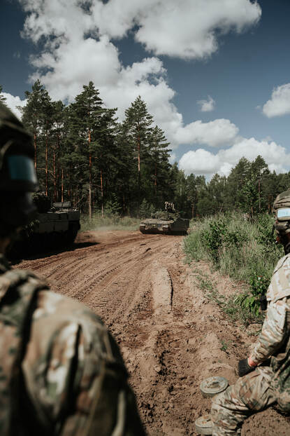 Twee CV90-infanteriegevechtsvoertuigen komen aangereden over een modderig pad in het bos.