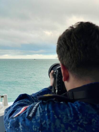 Een matroos neemt vanaf het dek foto’s van een ander schip.