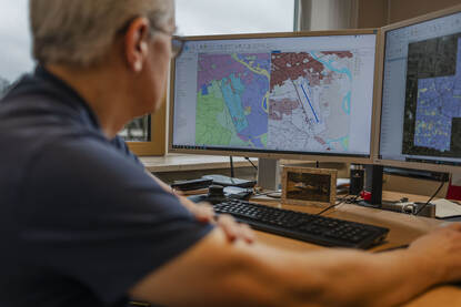 Een medewerker van de Dienst Geografie zit achter zijn computer en laat een kaart zien.