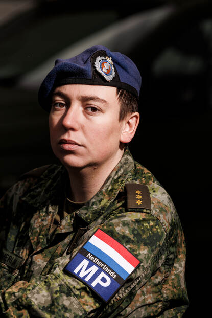Portretfoto van kapitein Eva met blauwe baret op en armpatches van de Militaire Politie en een Nederlandse vlag.