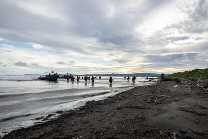 Links de Pelikaan op zee. Rechts waden mariniers vanaf een landingsboot naar het strand.