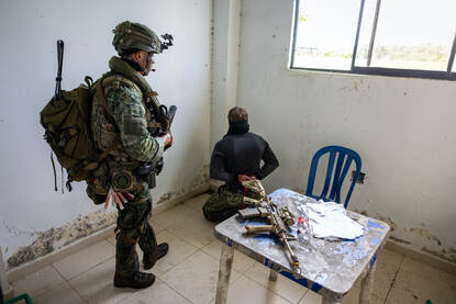 Links bewaakt een marinier een gevangengenomen vijand. Rechts een mouwembleem waarbij de Nederlandse en Colombiaanse vlag in elkaar overlopen.