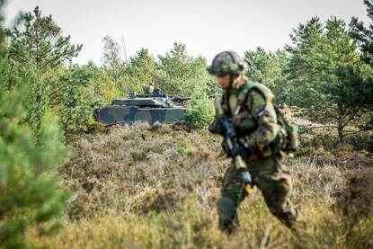 Militair te velde met op de achtergrond een voertuig.