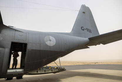 Staartdeel van een C-130 transportvliegtuig met laadklep omlaag. In deuropening staat iemand van de bemanning.