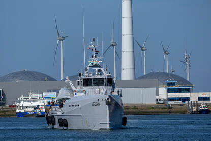 Boven het logo van Sandy Coast 2025 op de mouw van een marineman en duikondersteuningsvaartuig Zr.Ms. Nautilus aan de kade van Eemshaven. De DSS Galatea op zee en een rubber boot die over het water scheert.