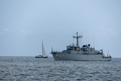 Boven: Op zee liggen een bootje van de marine en van de politie naast elkaar met de GeoSea op de achtergrond. Op de achterzijde van het bootje is de gele Seascan te zien. Daarna vaart de politie naast de Geosea. Onder: BNS Lobelia op zee en vervolgens gaat daarna een duikteami met een EOD’ers per rubber boot richting een mogelijk explosief.