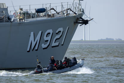 Boven: Op zee liggen een bootje van de marine en van de politie naast elkaar met de GeoSea op de achtergrond. Op de achterzijde van het bootje is de gele Seascan te zien. Daarna vaart de politie naast de Geosea. Onder: BNS Lobelia op zee en vervolgens gaat daarna een duikteami met een EOD’ers per rubber boot richting een mogelijk explosief.