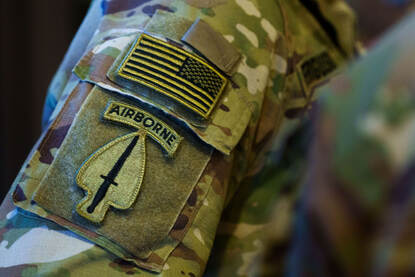 Viermaal een mouw van een militair uniform met daarop de vlaggen en logo’s van respectievelijk Nederland, de Verenigde Staten, het Verenigd Koninkrijk en Polen.