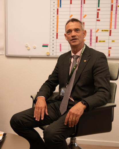 Man in pak praat vanuit stoel met achter hem een flipover.