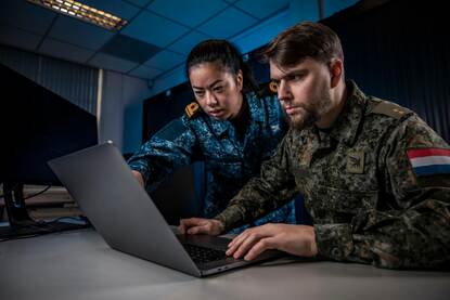 Links een digitaal slotje, rechts kijken twee militairen naar een laptopscherm.