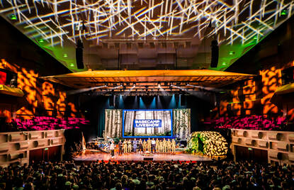 Volle theaterzaal met militairen op het podium.