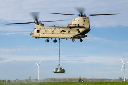 Een Chinook met een lading zakken hangt stil in een weiland.