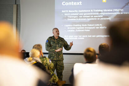 Op de linkerfoto geeft commandant Wesley een speech voor een groep toehoorders. Rechts laden militairen goederen in een vrachtwagen.