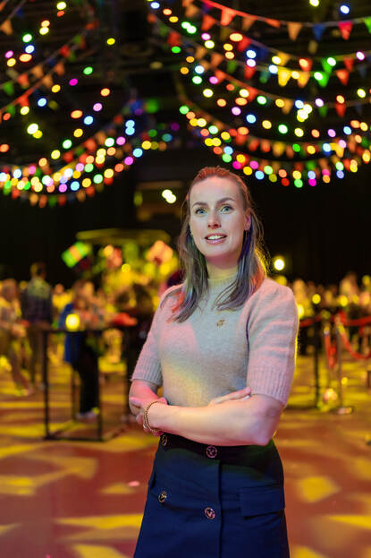 Vrouw staat met armen over elkaar in feestzaal.