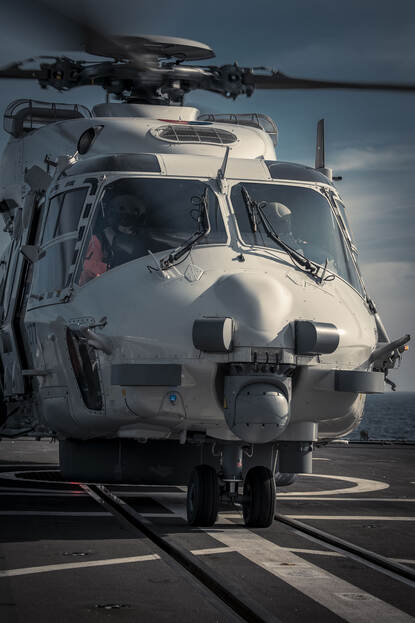 De NH90-boordhelikopter staat op het helidek van de Tromp. In de cockpit zitten 2 personen.
