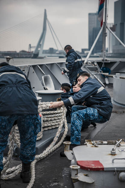 De nauten halen de trossen binnen. Op de achtergrond is de Erasmusbrug zichtbaar.