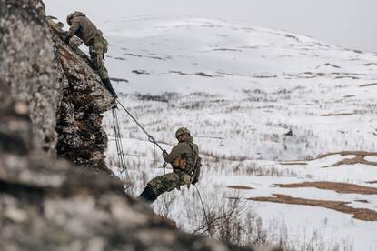 Mariniers dalen van een berg af in een besneeuwd landschap.