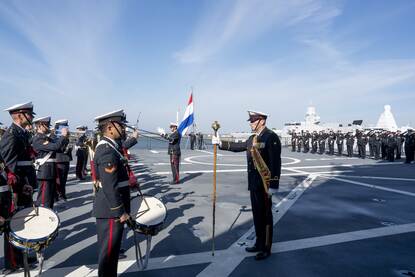 Genodigden zitten op stoelen op marineschip tijdens ceremonie en de muzikale begeleiding tijdens ceremonie.