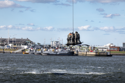 Op de linkerfoto vliegt een helikopter met eronder een soort mand, de AirTEP. Op de rechterfoto zijn operators in die mand geklommen.