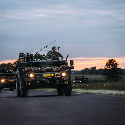 Een Fennek verkenningsvoertuig in de schemering, rijdend op de weg van een kazerne.