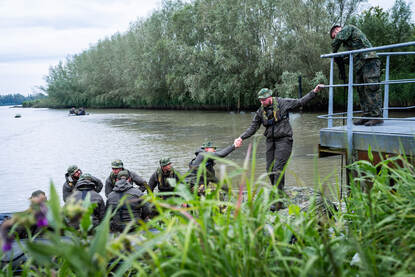 Een militair stapt van een steiger op de rubberboot, en krijgt de hand van een collega.