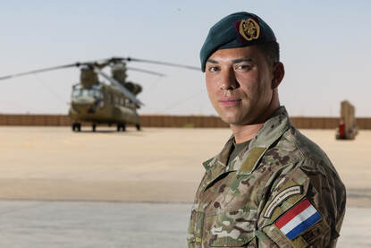 Majoor Henk kijkt in de lens van de camera. Achter hem staat een Chinook.