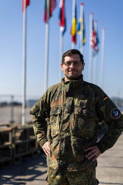 Luitenant-kolonel Benjamin poseert voor een rij vlaggen van alle deelnemende landen.