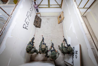 Vier militairen van bovenaf gezien die tijdens een oefening in een kamer hun wapens richten.