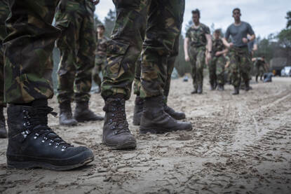 Links: close-up van benen en schoenen van militairen in gevechtstenue op zand. Rechts: jongeren in een groene overal op een hindernisbaan.