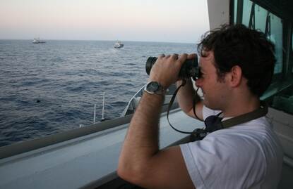 Foto links: Martijn tuurt vanaf een schip door zijn verrekijker. Foto rechts: Martijn met een slang om zijn nek in een tropisch bos.
