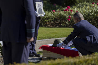 Militair legt helm op kist met daarover de Nederlandse vlag. Een andere militair toont er vlak boven een portretfoto van Beerschooten.