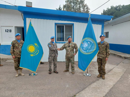 Majoor Beerens schudt hand van Kazachse militair, ernaast twee Kazachse militairen met vlaggen.