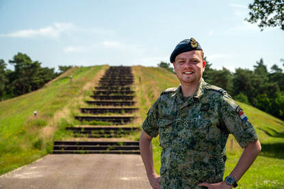Een militair staat met de handen in de zij voor een heuvel met daarop een lange trap naar boven.