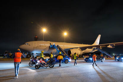 Militair transportvliegtuig op landingsbaan met motoragenten en auto's naast het toestel.