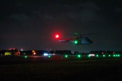Helikopter met groen en rood licht landt in het donker op vliegveld.