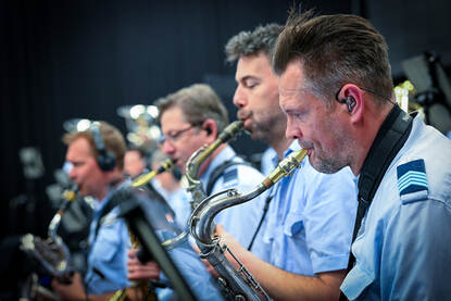 Vier orkestleden op een rij met een blaasinstrument in de mond.