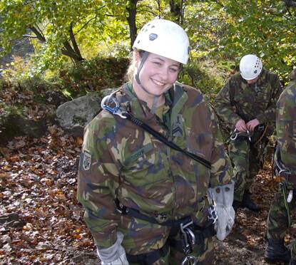 Karin in gevechtstenue met witte helm en klimgordel in een bos.